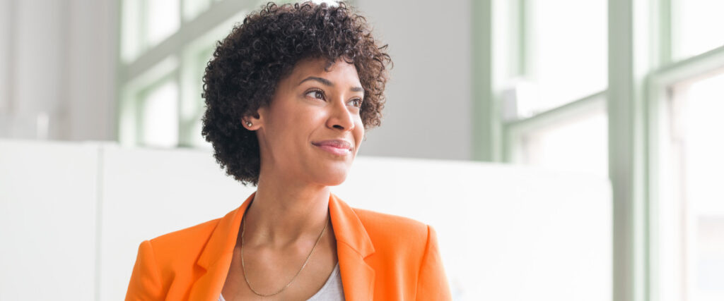 Confident woman in an orange jacket looking upward with a sense of clarity and purpose, representing self-mastery and soul-aligned living.